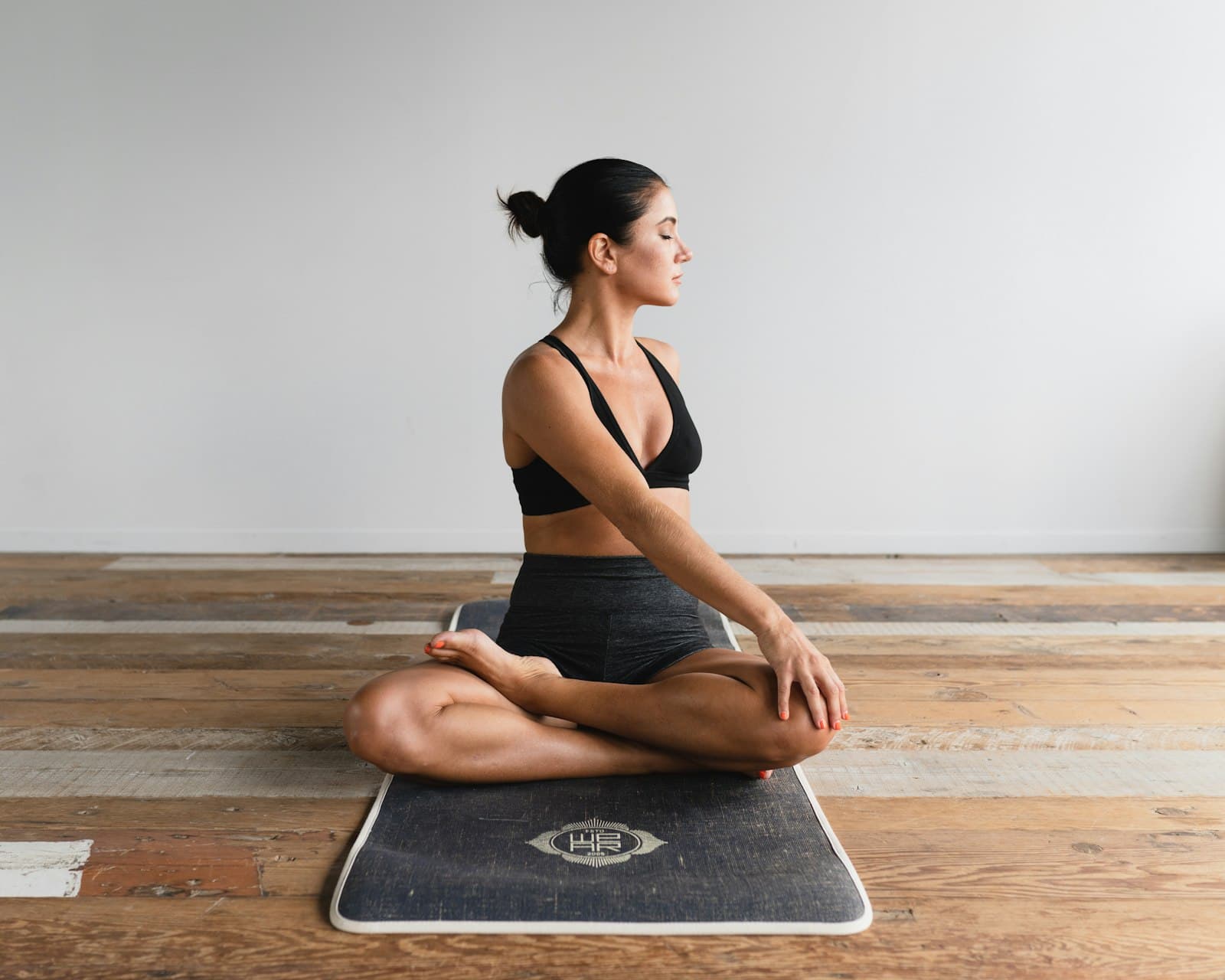 A member holding a seated twist on a mat, on a timber floor in soft daylight